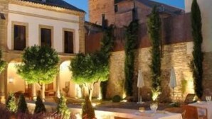 An outdoor dining area with tables and chairs, a stone wall, and a bell tower in the background. - Hotel Puerta de la Luna (Baeza)