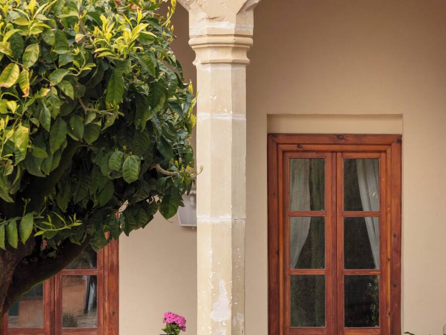 Un arco de piedra que da a una puerta de madera, una mesa con dos sillas y una planta en maceta.