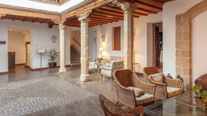 A spacious interior with a high ceiling, exposed wooden beams, stone columns, and wicker furniture. - Hotel Puerta de la Luna (Baeza)