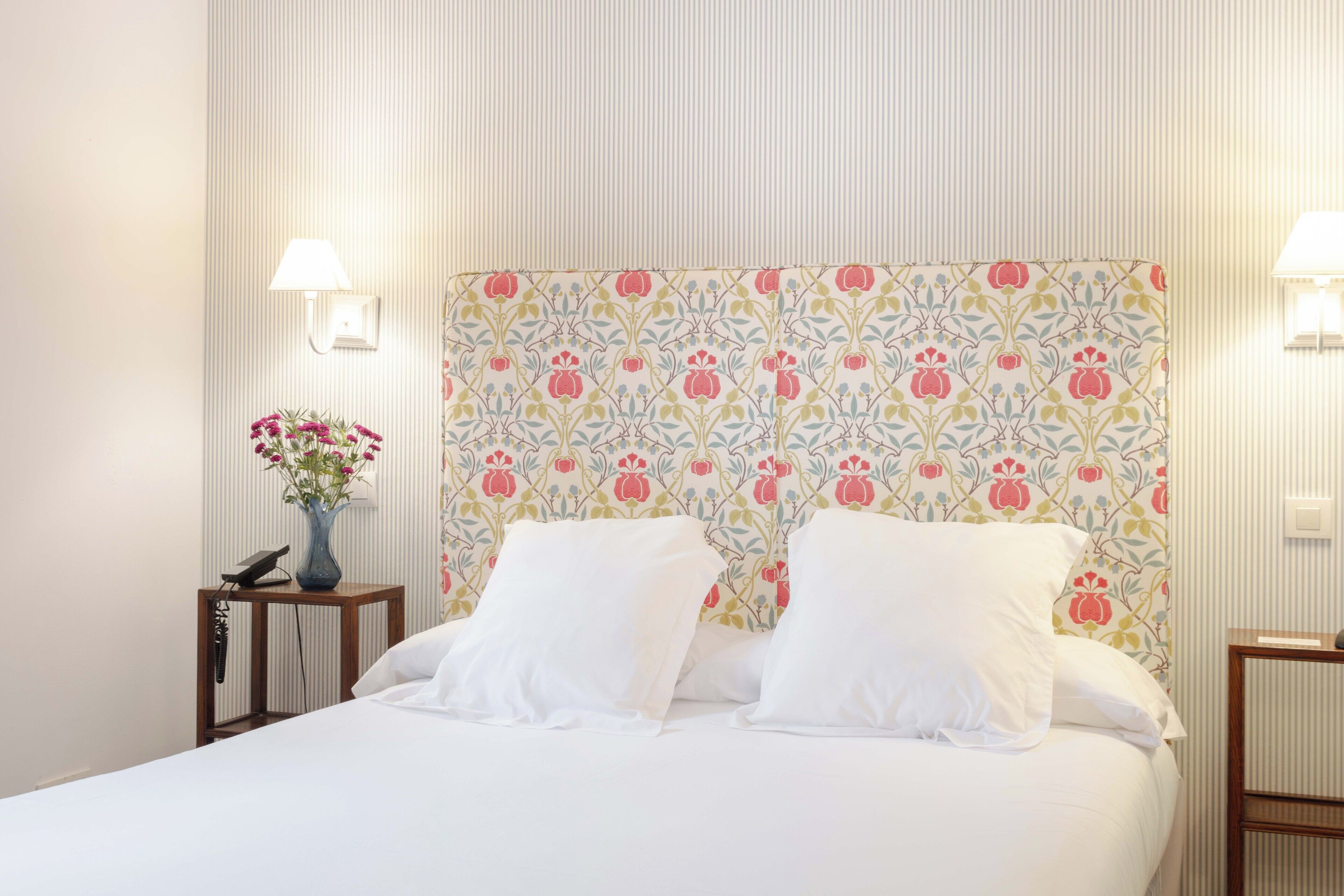A neatly made bed with white linens, a floral-patterned headboard, and bedside lamps.