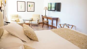 A hotel room with a bed, two chairs, a desk, a television, and framed pictures on the wall.