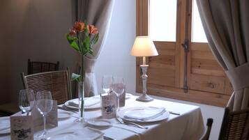 A dining table set for two with a vase of flowers, a menu, and a candle.