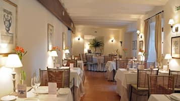 Un restaurante con varias mesas dispuestas, cubiertas con manteles blancos, sillas y cristalería.