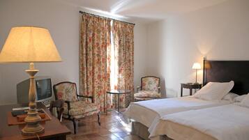 Habitación de hotel con dos camas, un escritorio con lámpara, una silla, una mesita y cortinas.