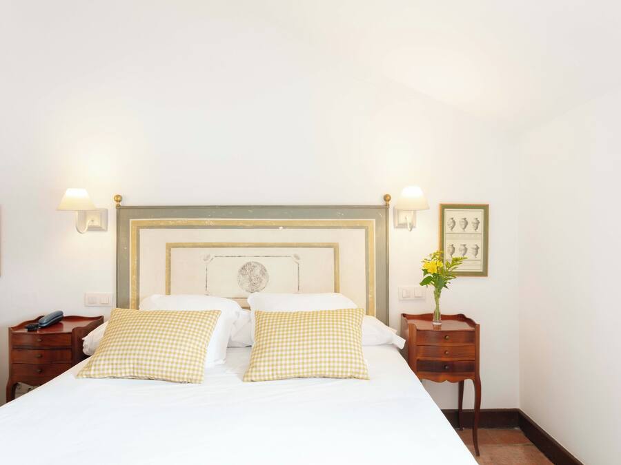 A neatly made bed with checkered pillows, a wooden headboard, and bedside tables with lamps and framed pictures.