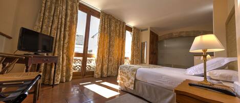 A hotel room with a bed, a desk with a television, a lamp, and a view of the outside.
