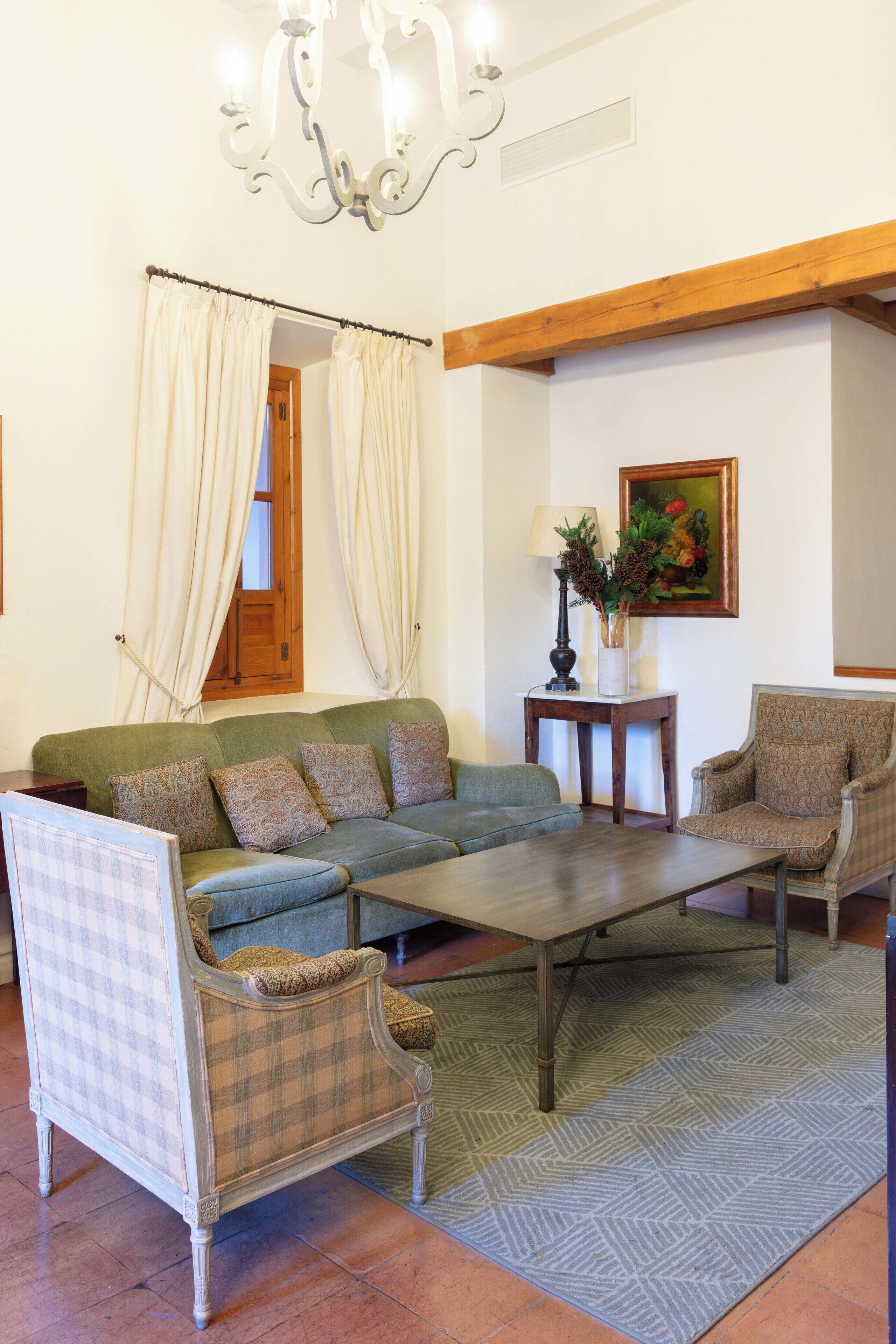 Una sala de estar con sofá, sillones, una mesa de centro, una lámpara y un cuadro en la pared.