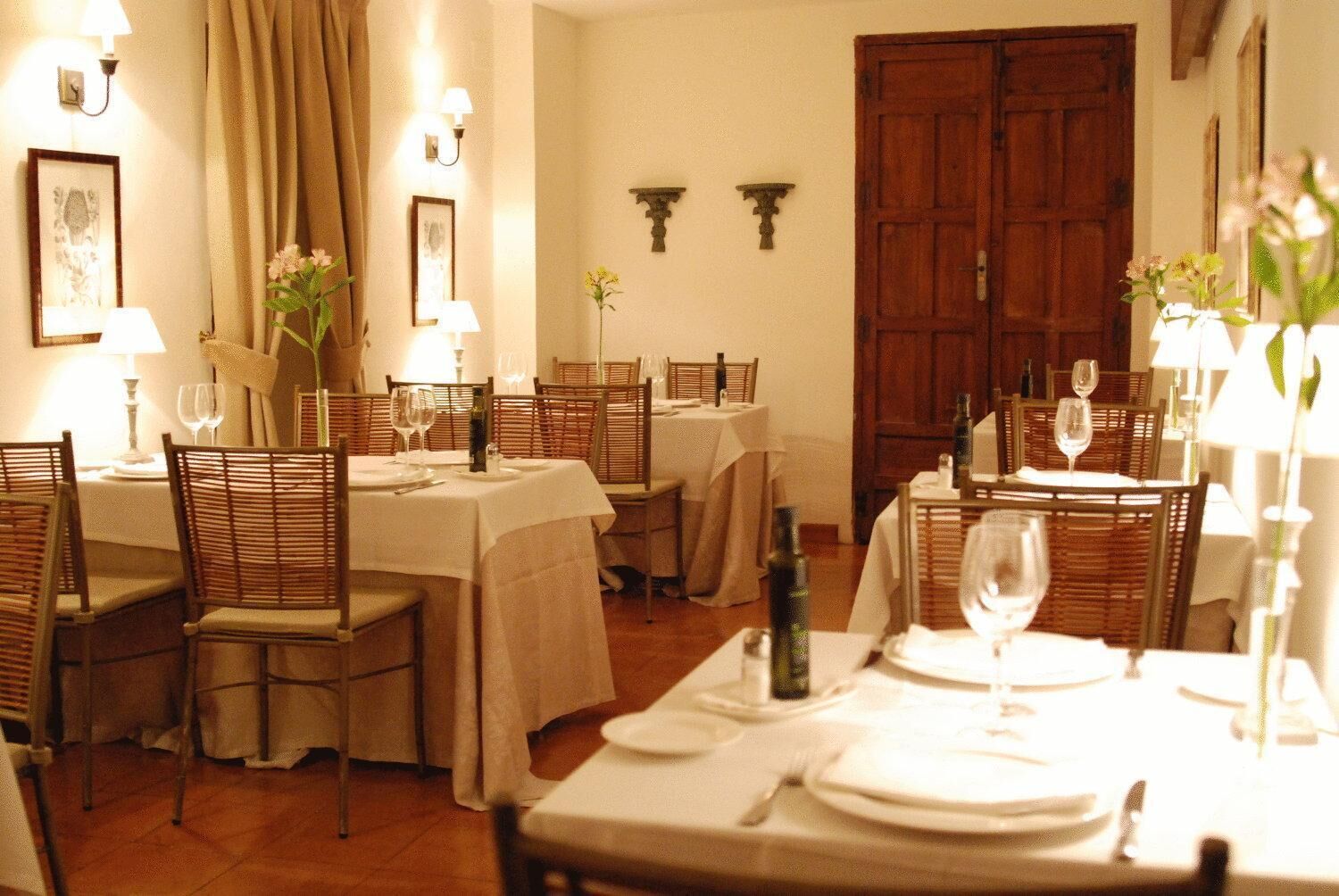 Comedor con mesas dispuestas para dos, sillas de madera y lámparas fijadas a la pared.