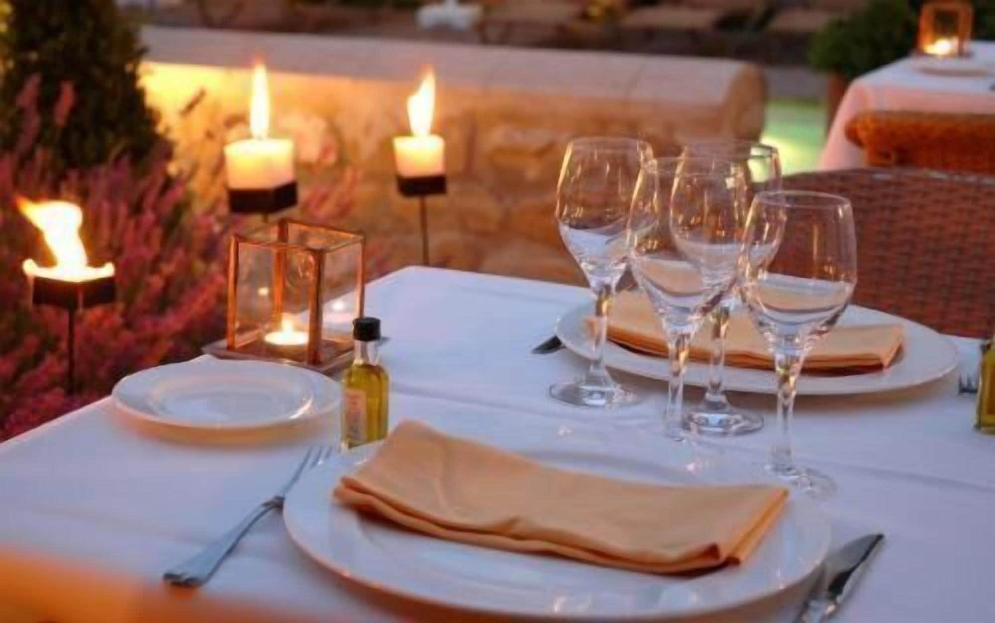 Ein Tisch, gedeckt für eine Mahlzeit, mit Kerzen, Gläsern und einer Olivenölflasche.