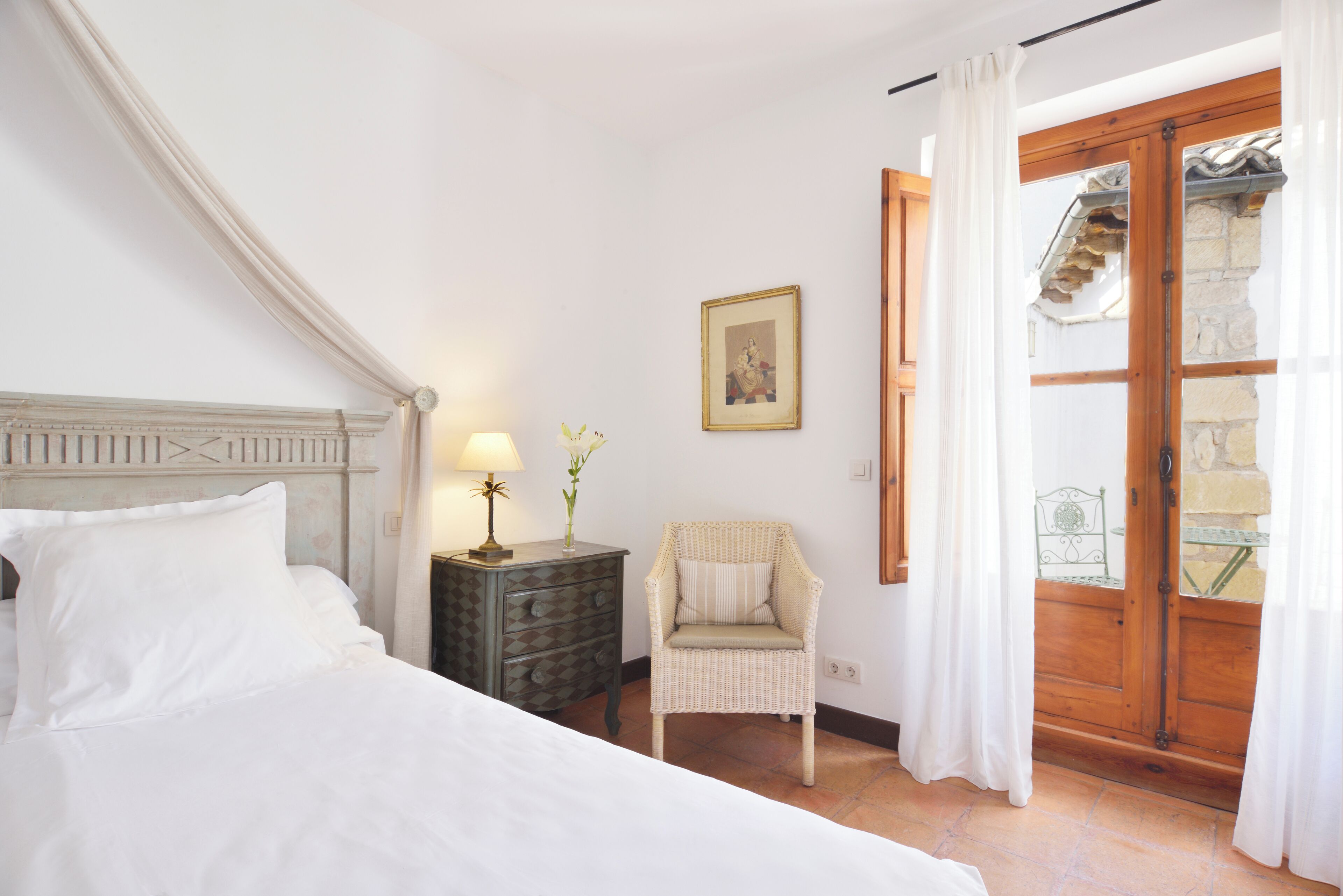 A bedroom with a bed, a nightstand, a chair, and a window with curtains.