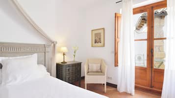 A bedroom with a bed, a nightstand, a chair, and a window with curtains.