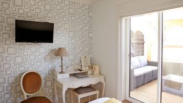 A room with a patterned wall, a flat-screen TV, a desk with a lamp, a chair, and a bed.