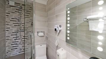 A modern bathroom with a glass-enclosed shower, a toilet, a vanity with a mirror, and a hand dryer.
