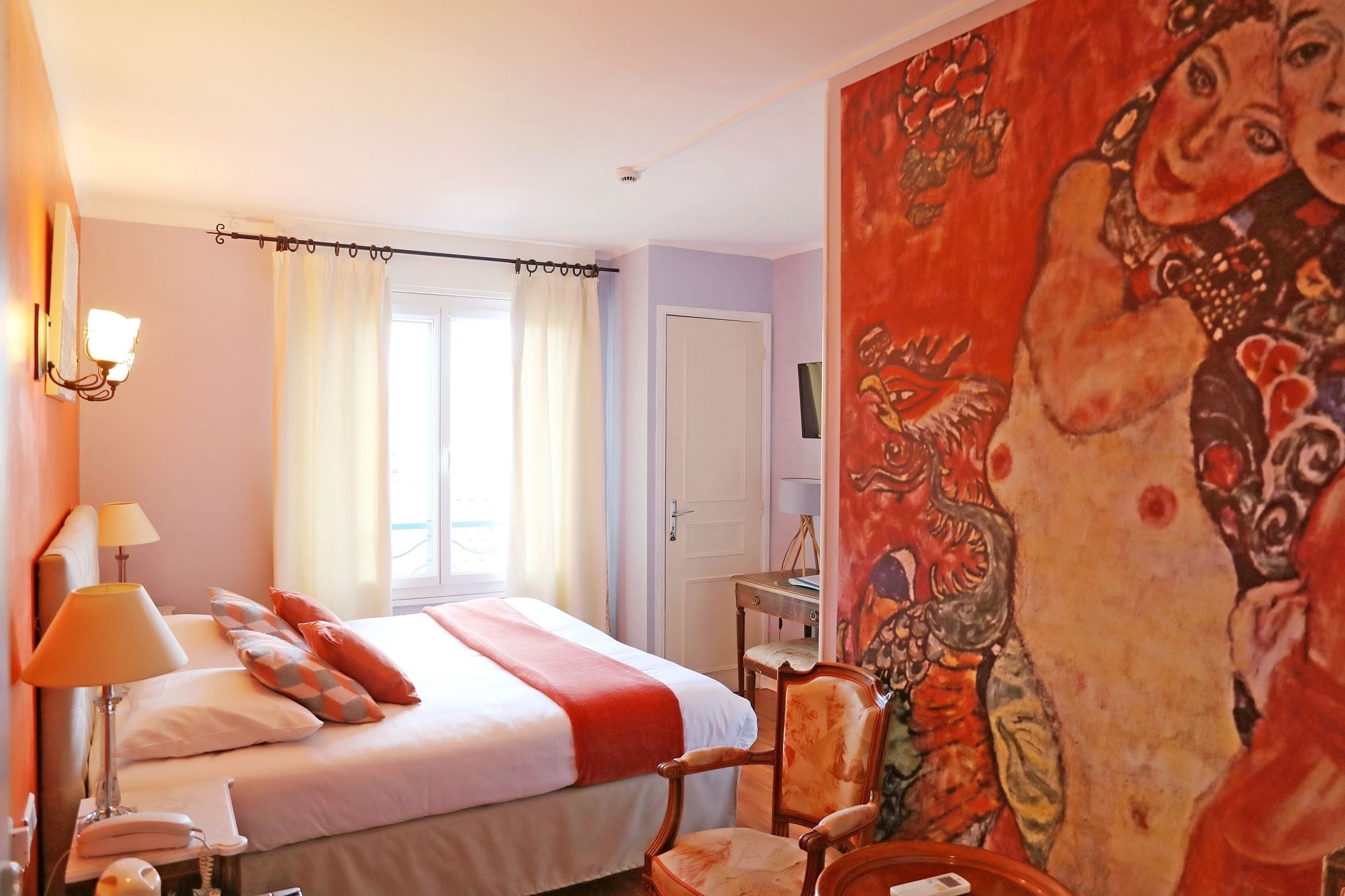 A hotel room with a bed, a chair, a desk, and a painting on the wall.