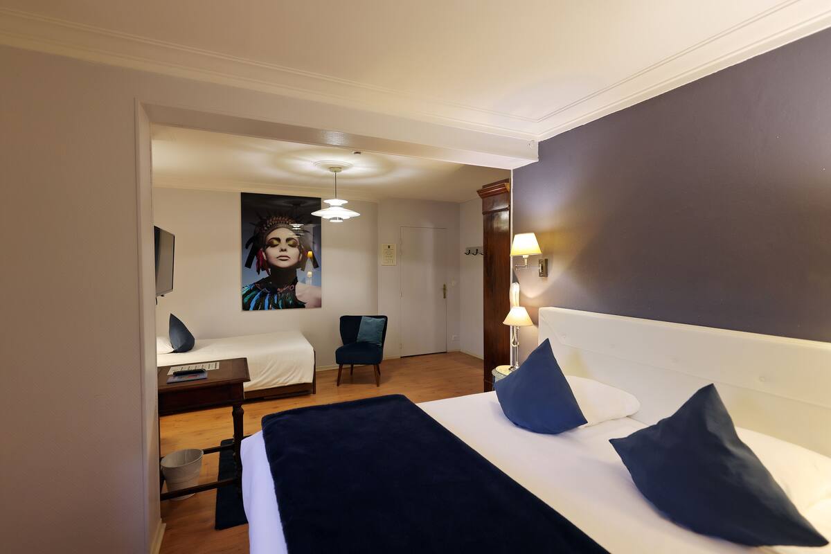 A hotel room with a bed, a chair, a desk, and a lamp.