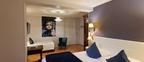 A hotel room with a bed, a chair, a desk, and a lamp.