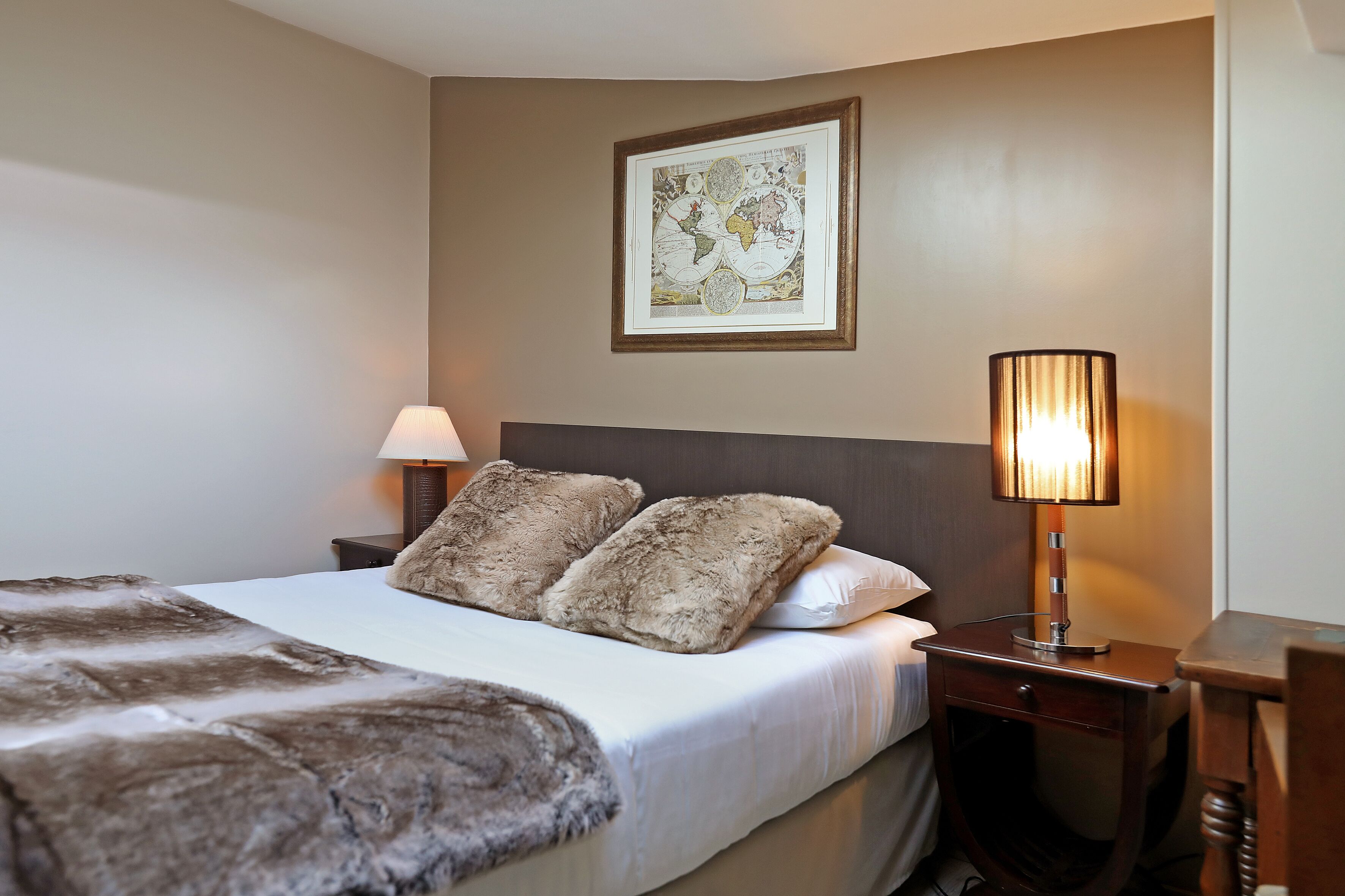 A hotel room with a large bed, two pillows, a lamp, and a framed map on the wall.