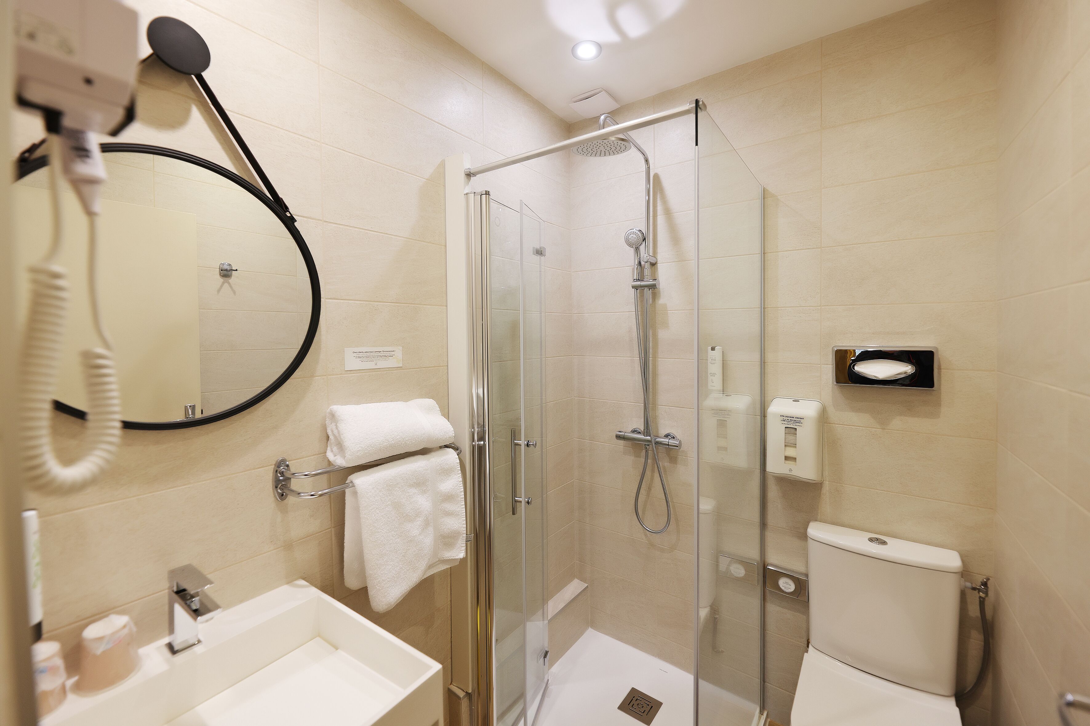 Un baño moderno con ducha de vidrio, lavamanos con espejo e inodoro.