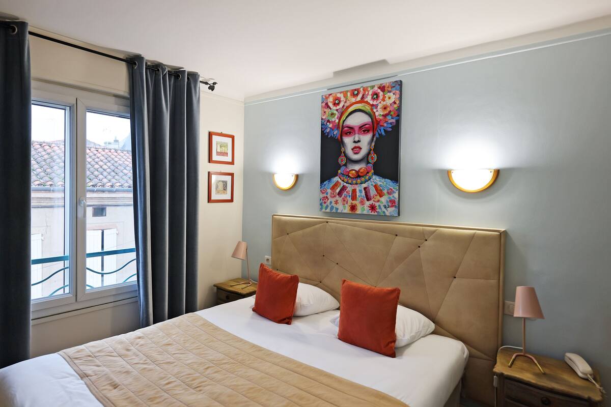 A hotel room with a large bed, two pillows, a headboard, bedside lamps, a nightstand, a phone, and a painting on the wall.