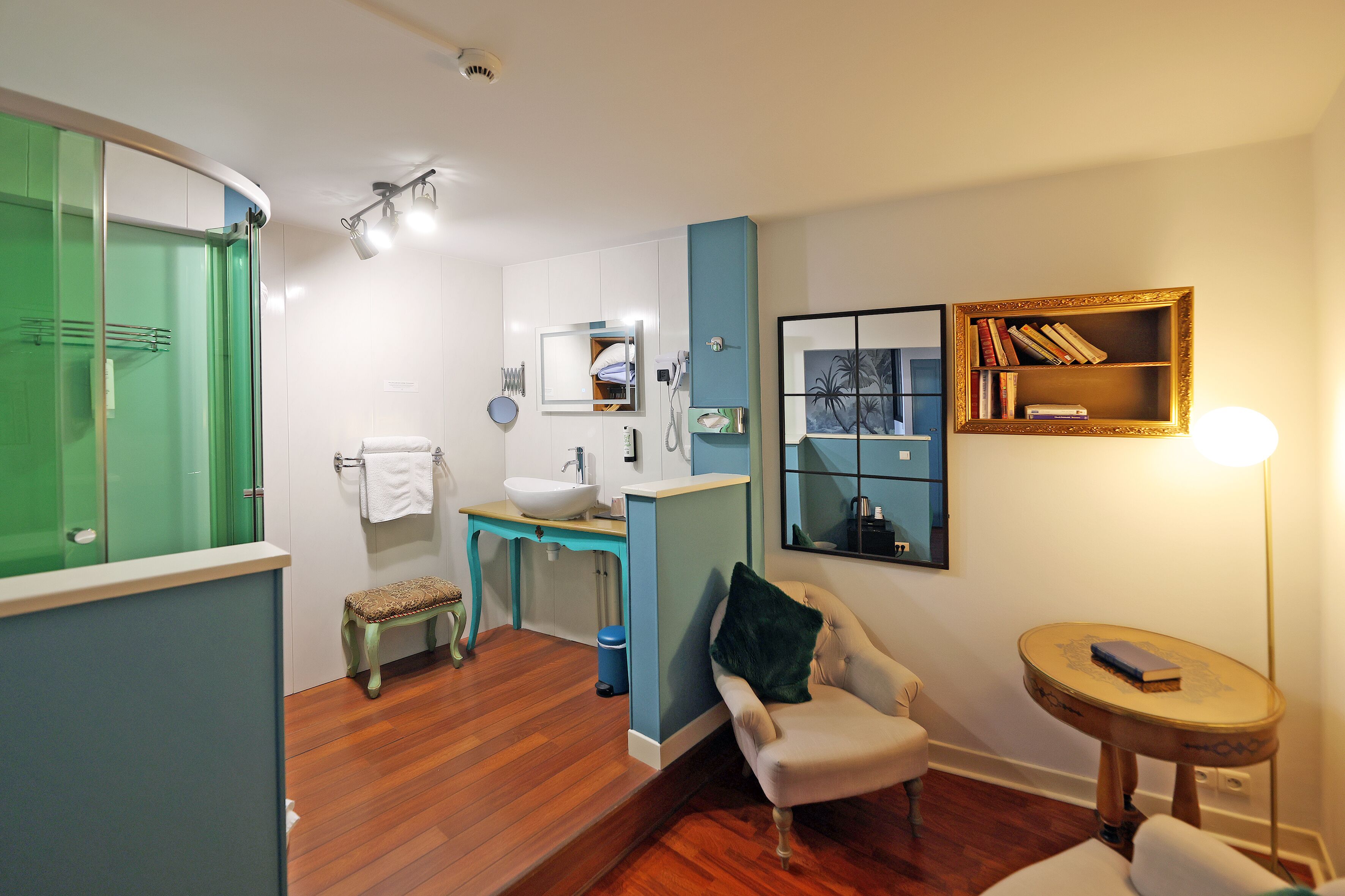 Un baño con una puerta verde, un lavabo, una banca, una silla y una pequeña mesa con un libro.