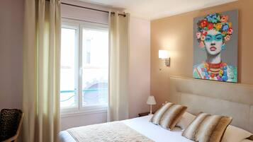 Habitación de hotel con una cama, una silla, un cuadro y una ventana con cortinas.