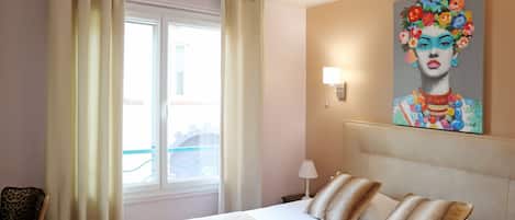 Een hotelkamer met een bed, een stoel, een schilderij en een raam met gordijnen.