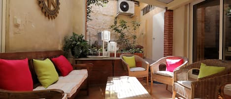 A sunlit patio with wicker furniture, a wooden table, and a wall-mounted fan.