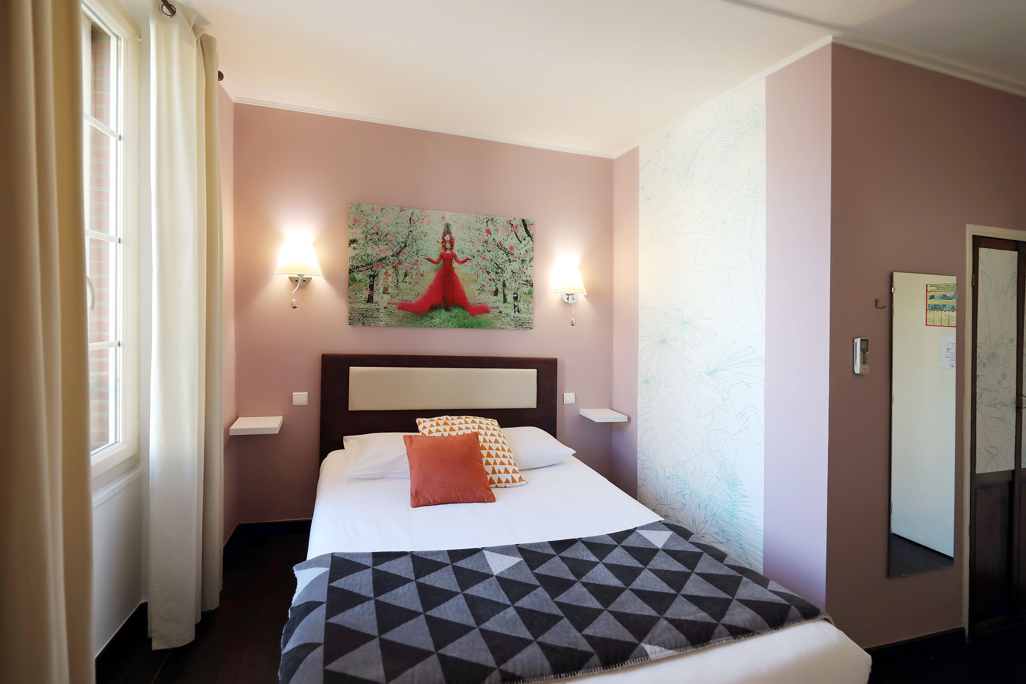 A hotel room with a bed, a painting on the wall, a nightstand, and a mirror.