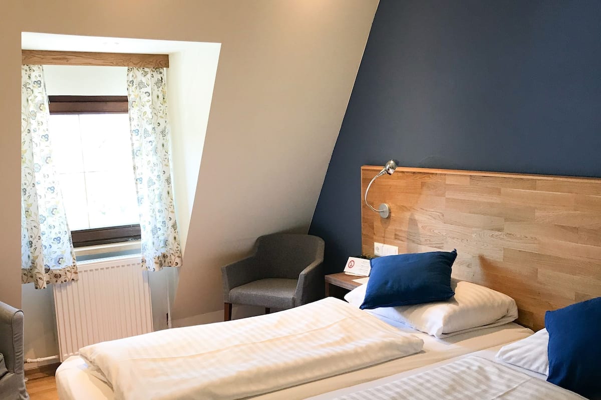 A bedroom with two beds, a chair, a radiator, and a window with curtains.