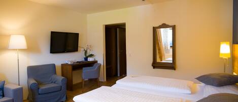 Habitación de hotel con cama, escritorio, silla, televisor y espejo.