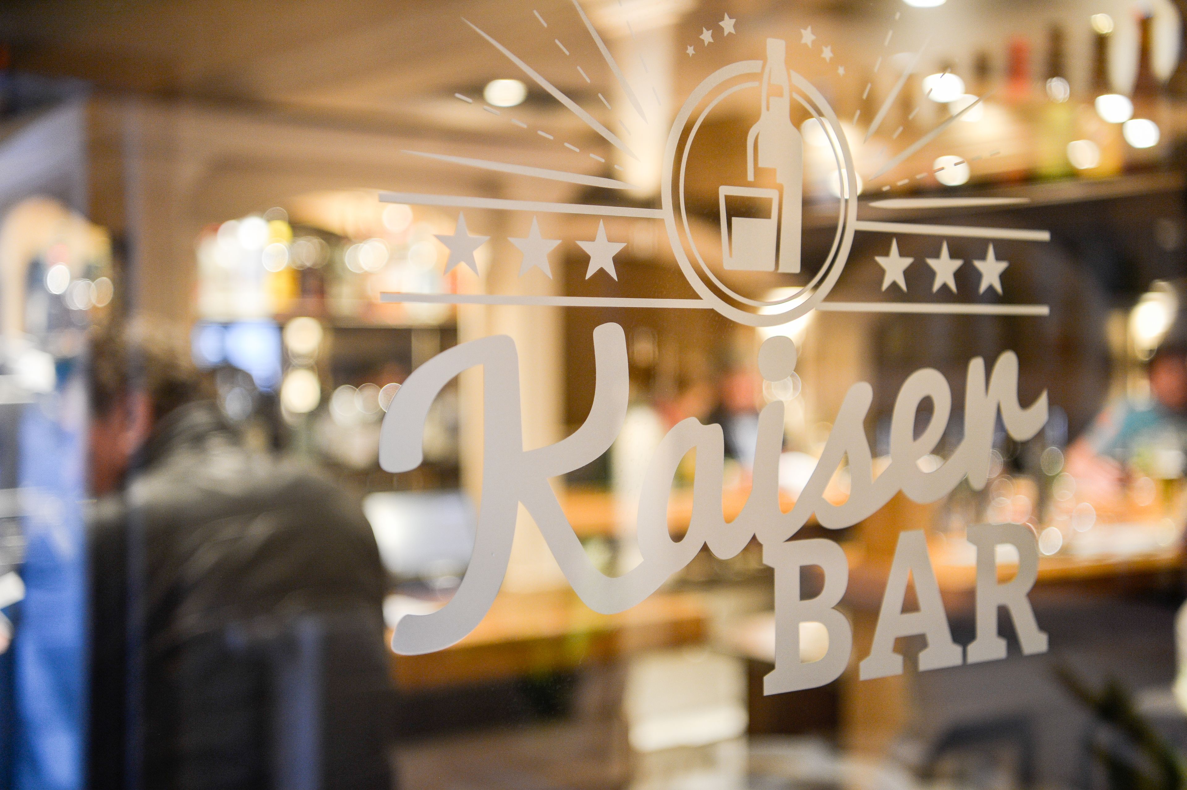 A bar sign with a bottle and stars, indicating a bar named "Kaiser BAR".