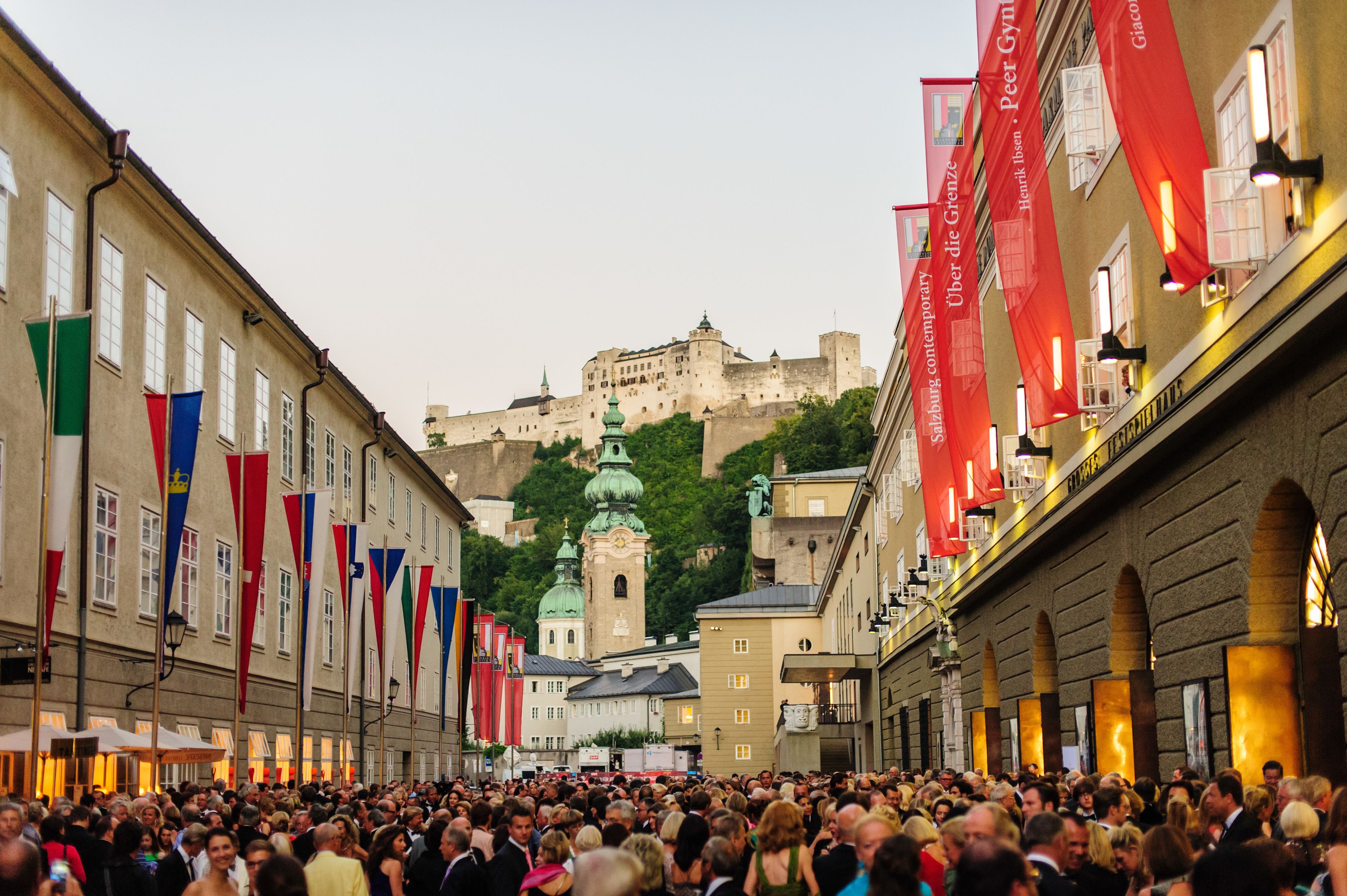A crowded street with historic buildings and a castle in the background.