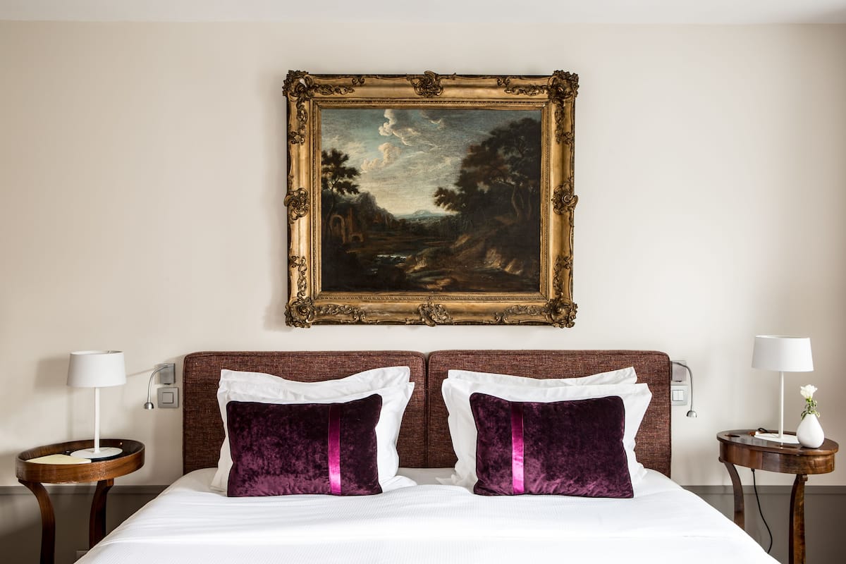 A hotel room with a bed, two nightstands, a painting on the wall, and a lamp on each nightstand.