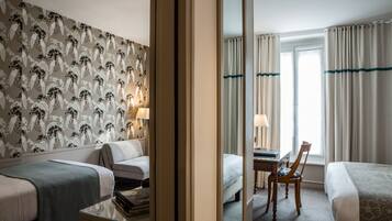A hotel room with two beds, a desk with a chair, a mirror, and a window with curtains.
