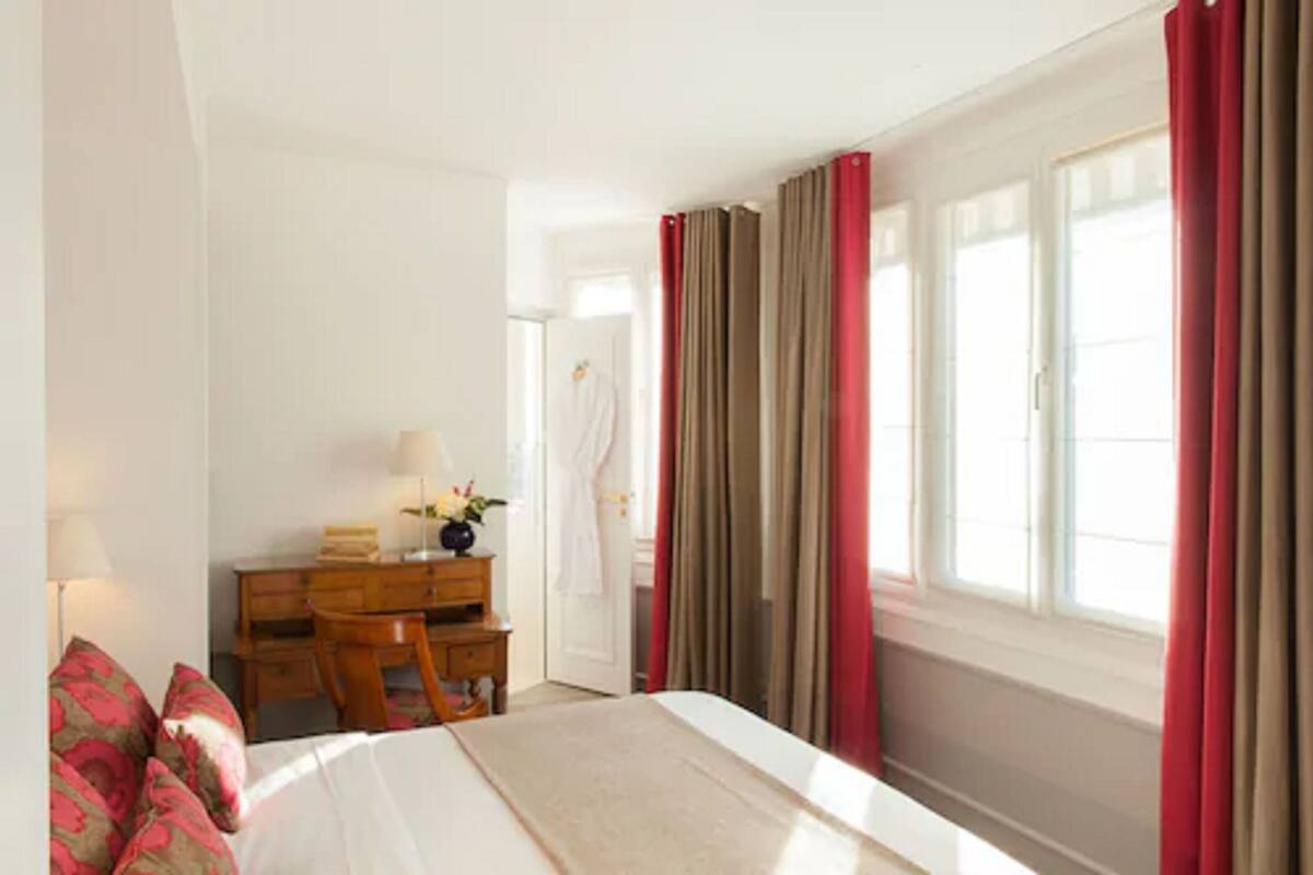 A hotel room with a bed, a desk, and a chair. There is a window with curtains, and a door leading to another room.