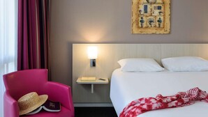Habitación de hotel con cama, mesita de noche, lámpara, silla y una obra de arte en la pared.