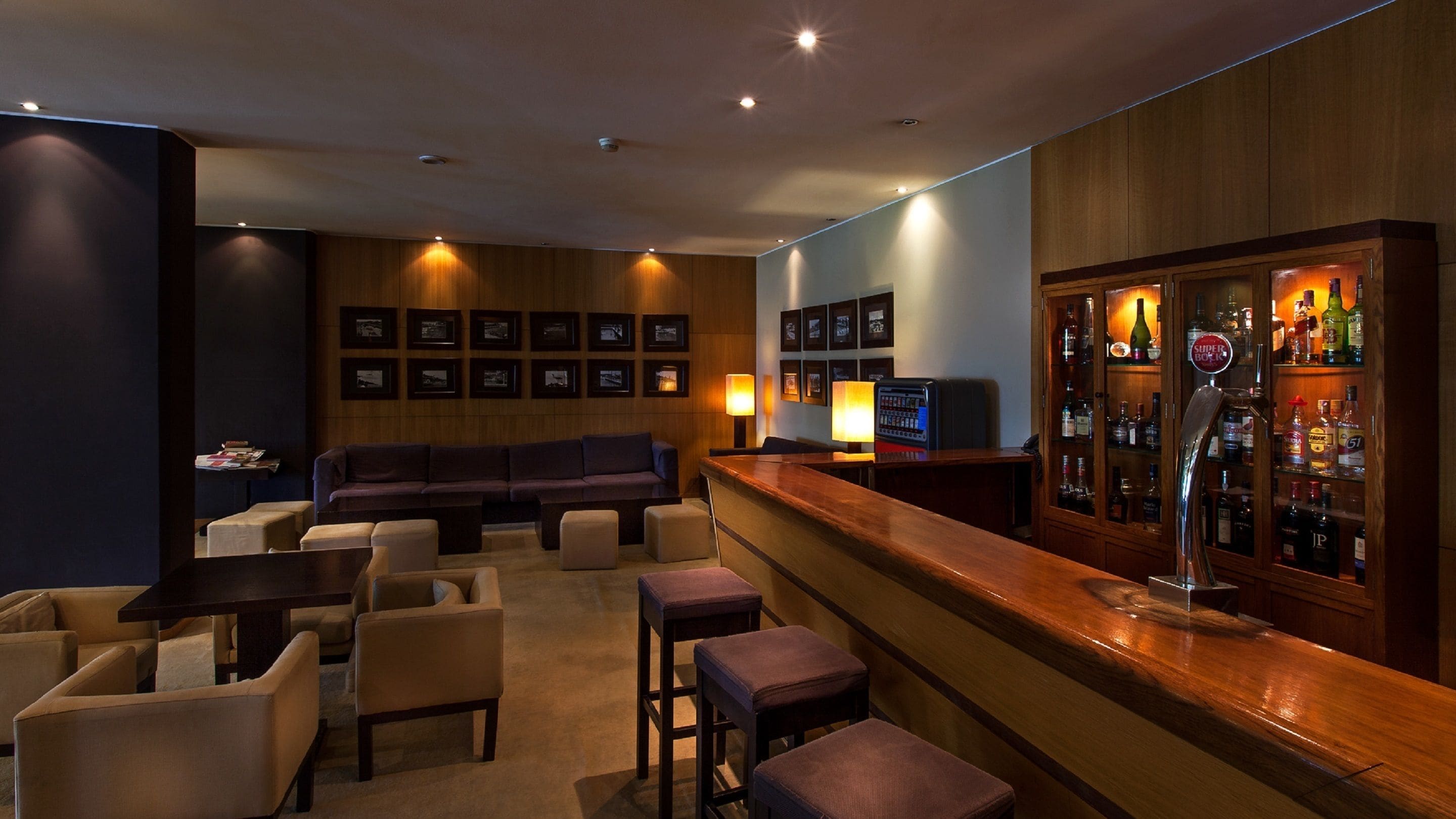 Una zona de bar con mostrador de madera, taburetes, un sofá y una pared de cuadros enmarcados.