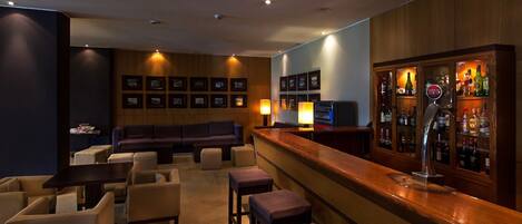 Una zona de bar con mostrador de madera, taburetes, un sofá y una pared de cuadros enmarcados.