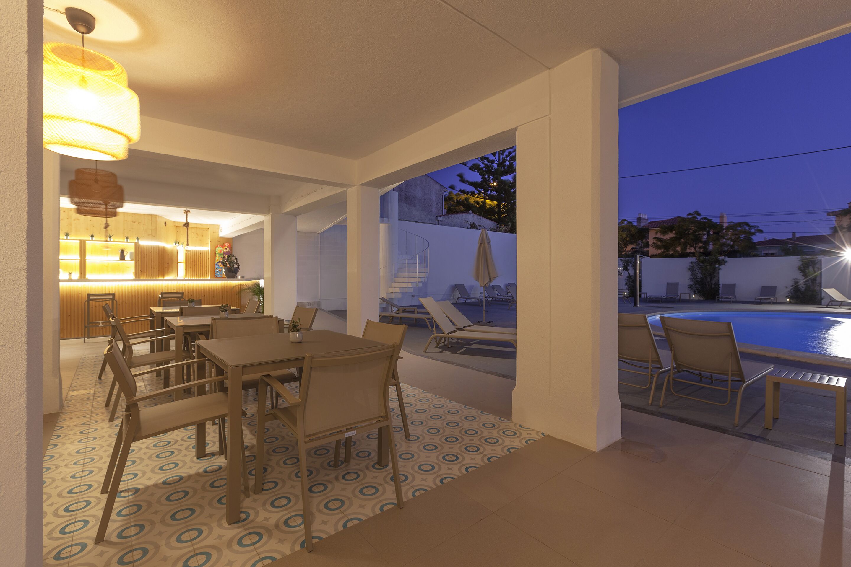 A modern outdoor dining area with a pool view, a kitchen with warm lighting, and a patterned floor.