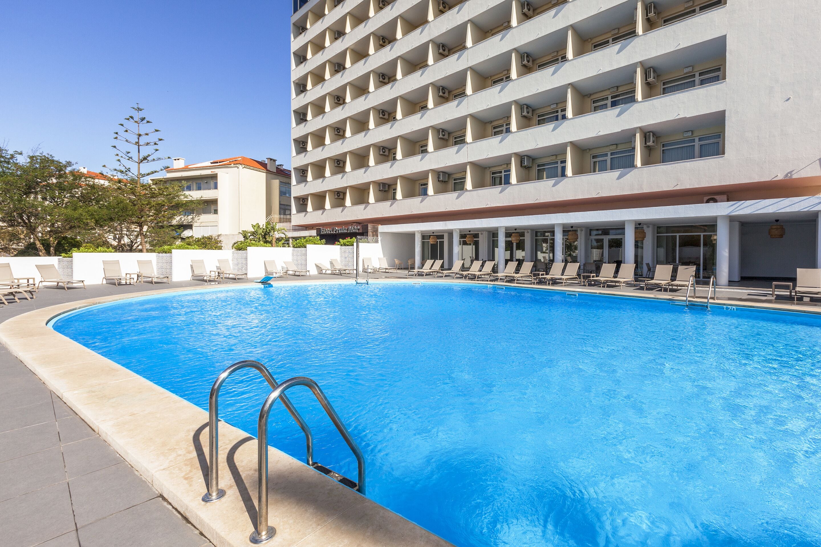 Une piscine à l’eau d’un bleu cristallin, entourée de chaises longues et bordée d’un bâtiment doté de nombreux balcons.
