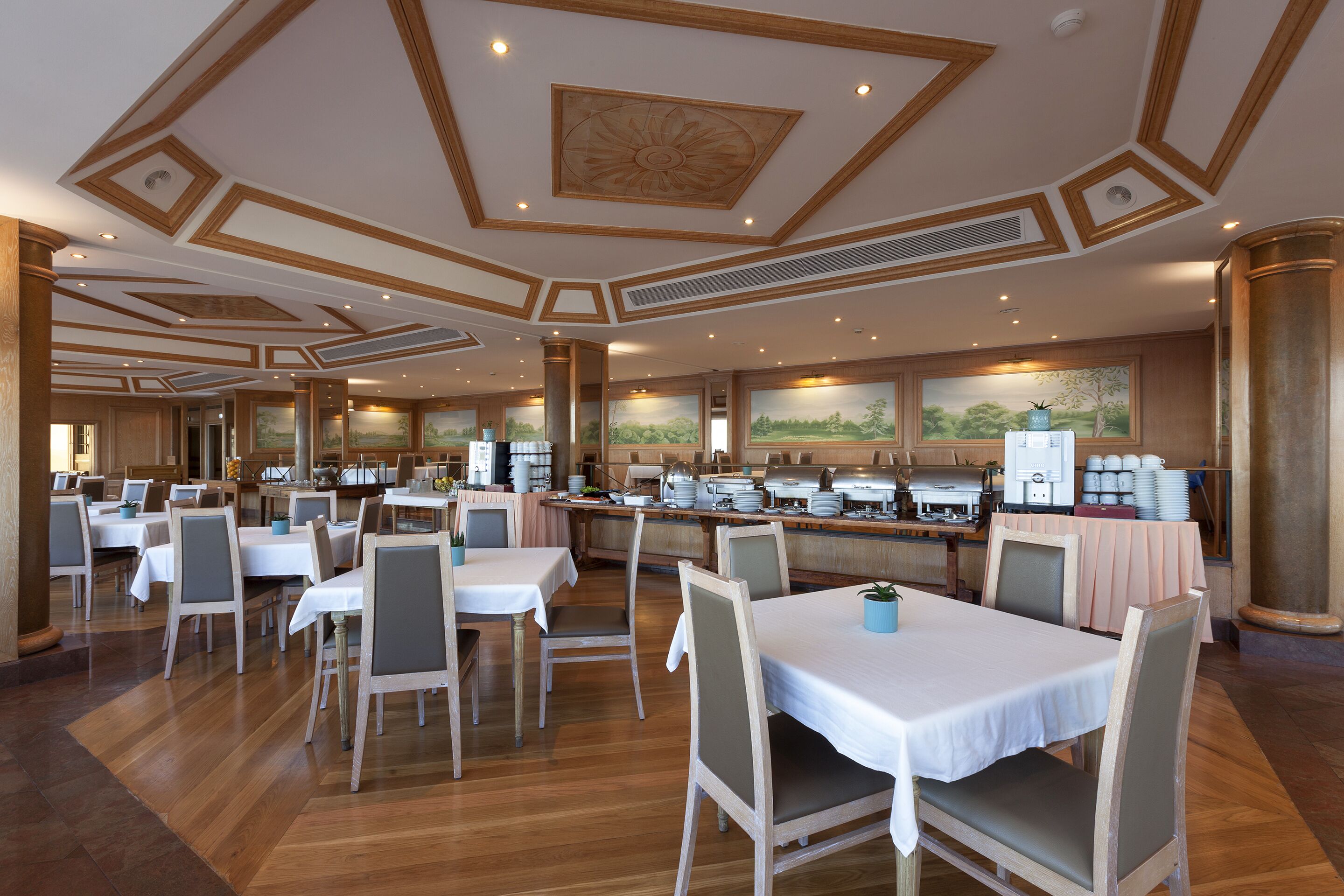 A spacious dining area with multiple tables and chairs, a buffet setup, and a large mural on the wall.