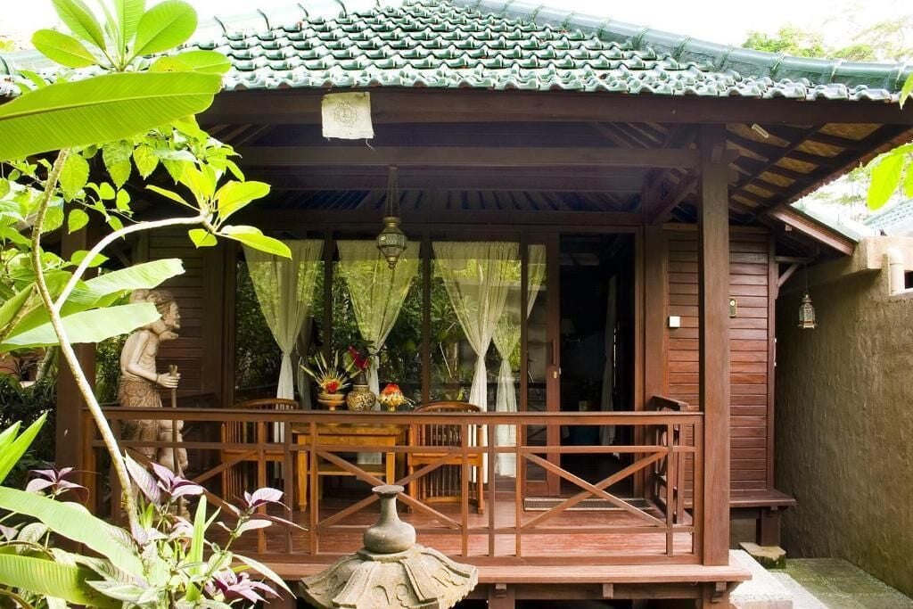 A wooden structure with a tiled roof, a covered porch, and a stone statue.