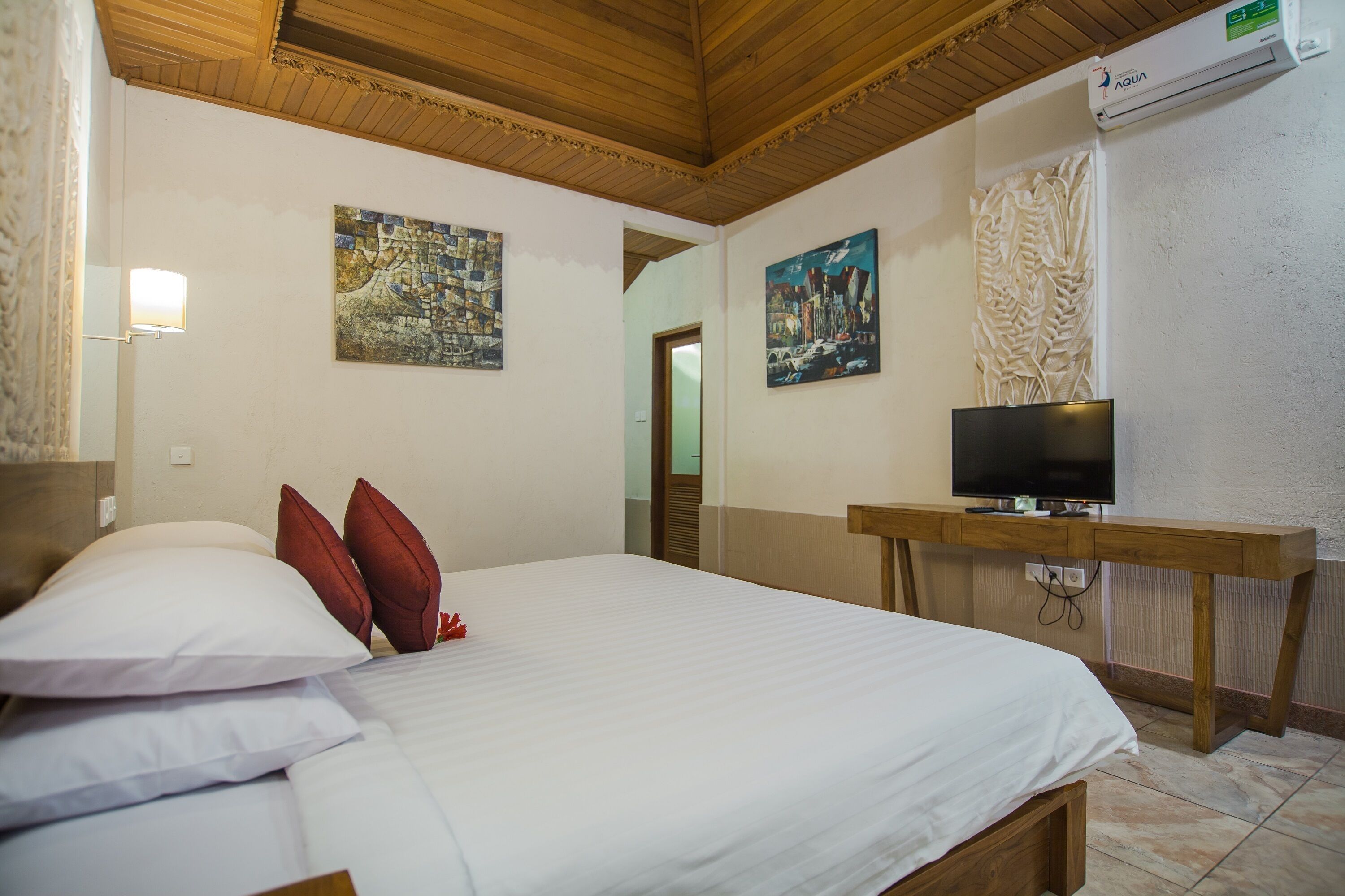 A hotel room with a bed, pillows, a TV on a wooden desk, and two paintings on the walls.
