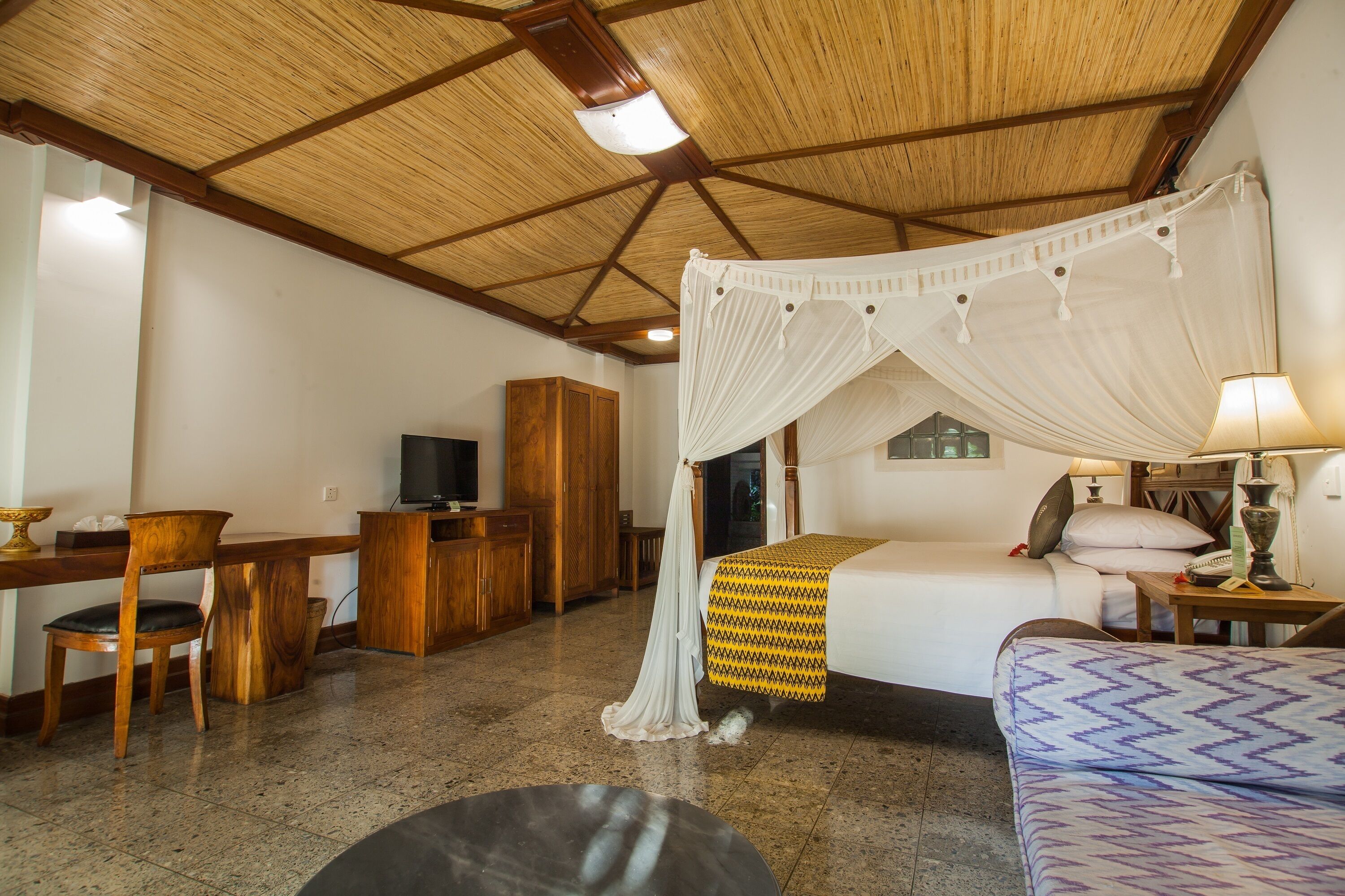 A room with a bed, a desk, a chair, a television, and a canopy bed.