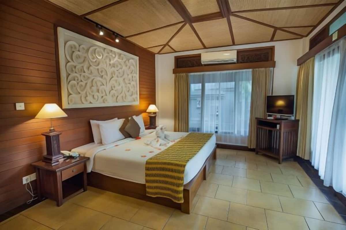 A hotel room with a bed, bedside lamps, a TV, a decorative wall piece, and an air conditioning unit.