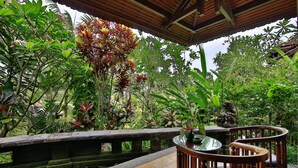 A covered outdoor seating area with a stone bench, surrounded by lush greenery and a stone statue. - Bali Spirit Hotel & Spa (Ubud)