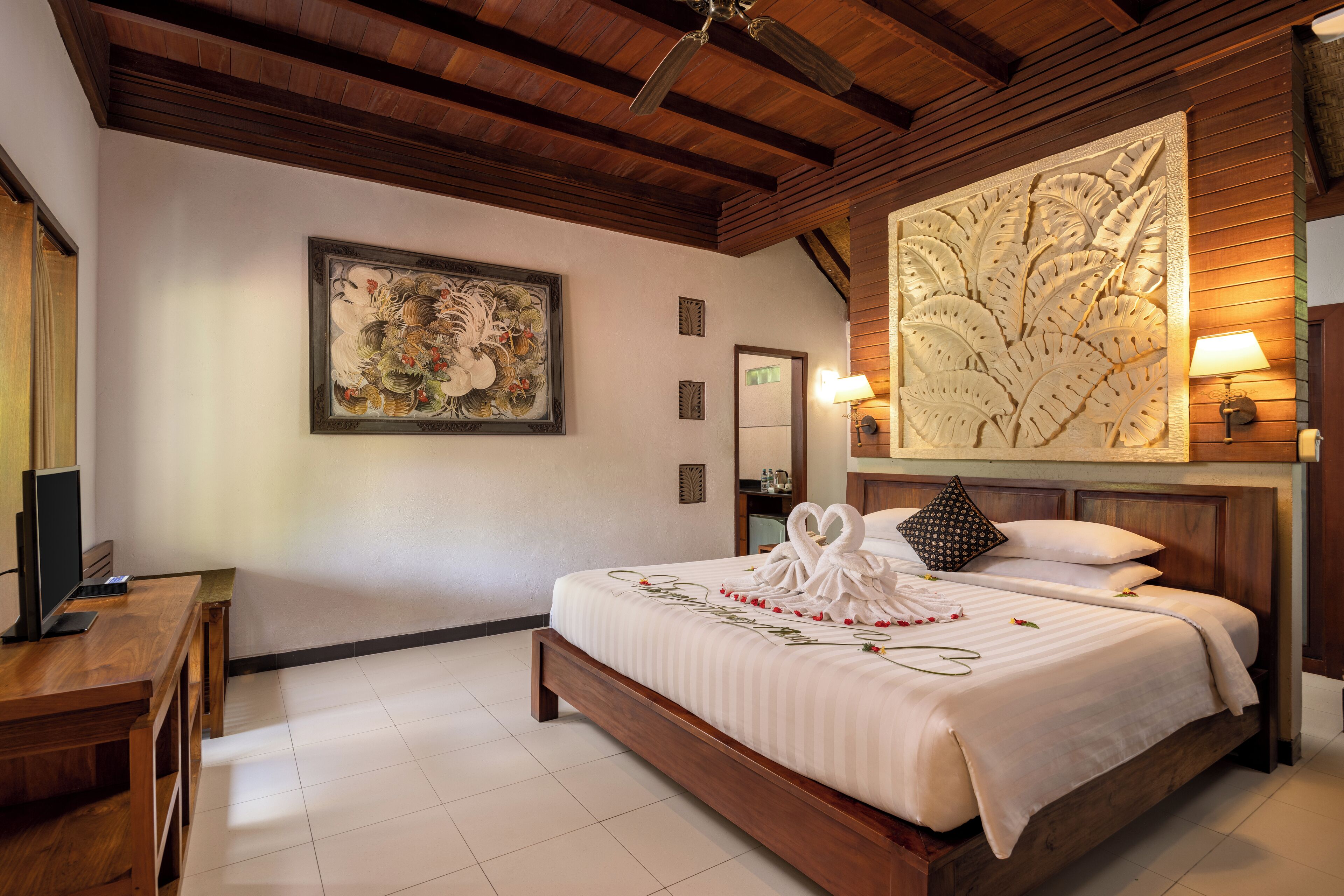 Quarto de hotel com cama de madeira, uma grande obra de arte na parede, escrivaninha e televisão.