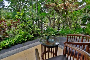 A glass-top table with a vase, surrounded by lush greenery and a wooden chair. - Bali Spirit Hotel & Spa (Ubud)