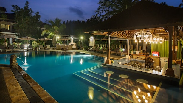 A swimming pool with lounge chairs and umbrellas, a bar area with a drink station, and a covered seating area with a decorative light fixture. - Bali Spirit Hotel & Spa (Ubud)