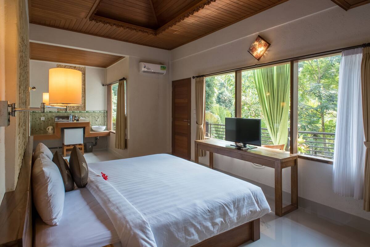 A hotel room with a bed, a desk with a computer, a mirror, and a window with curtains.